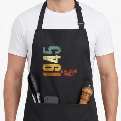 Tablier de cuisine noir avec chiffres 1945 vert jaune orange et texte Le Millésime Parfait en rouge.