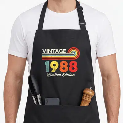 Tablier de cuisine noir avec inscription vintage 1988 Limited Edition et motifs rétro colorés sur le devant.