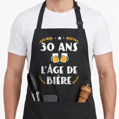 Tablier de cuisine noir avec inscription 30 ans l'âge de bière et deux verres de bière s'entrechoquant au centre.