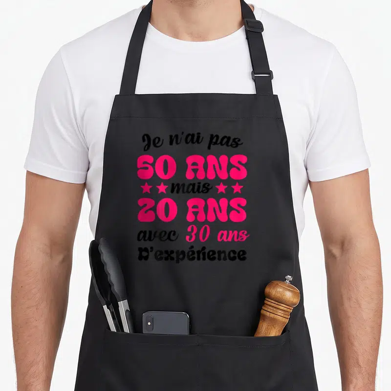Tablier de cuisine noir avec le texte Je n'ai pas 50 ans mais 20 ans avec 30 ans d'expérience en rose vif et noir.