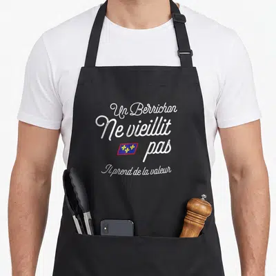 Tablier de cuisine noir avec texte blanc Un Berrichon ne vieillit pas et drapeau berrichon coloré au centre.
