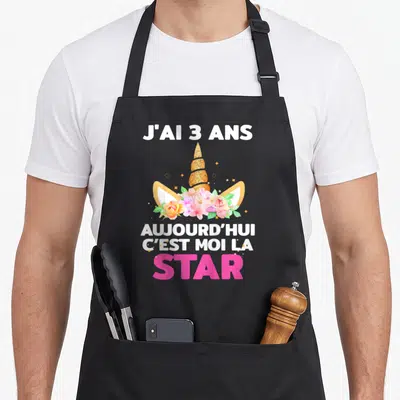 Tablier de cuisine noir avec motif licorne, cornes dorées, couronne de fleurs roses et texte blanc et rose.