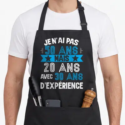 Tablier de cuisine noir avec le texte Je n'ai pas 50 ans mais 20 ans avec 30 ans d'expérience en bleu et blanc.