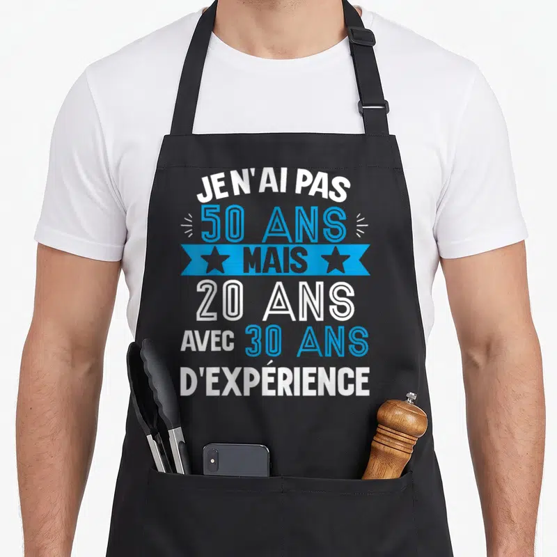 Tablier de cuisine noir avec le texte Je n'ai pas 50 ans mais 20 ans avec 30 ans d'expérience en bleu et blanc.