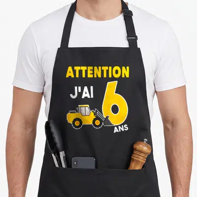 Tablier de cuisine noir avec attention j'ai 6 ans et illustration de pelleteuse jaune sur le devant.