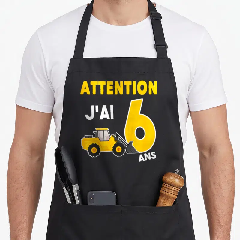 Tablier de cuisine noir avec attention j'ai 6 ans et illustration de pelleteuse jaune sur le devant.