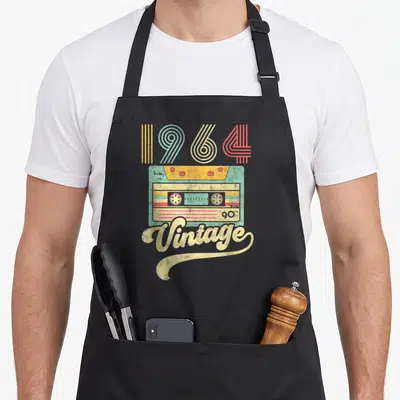 Tablier de cuisine noir avec illustration vintage d'une cassette audio et l'année 1964 en lettres colorées.