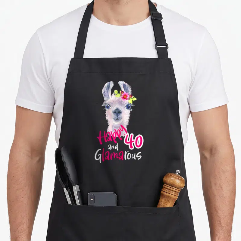 Tablier de cuisine noir avec illustration d'un lama portant des fleurs et le texte Happy 40 and Glamarous en rose et blanc.