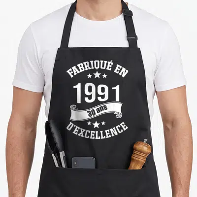 Tablier de cuisine noir avec inscription Fabrique en 1991 30 ans d'excellence et décorations étoilées blanches.