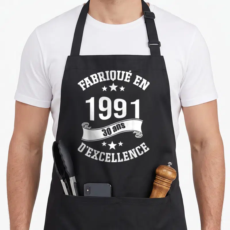 Tablier de cuisine noir avec inscription Fabrique en 1991 30 ans d'excellence et décorations étoilées blanches.