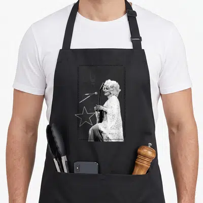 Tablier de cuisine noir avec illustration monochrome de Dolly Parton tenant une guitare sous le texte Légende de la musique country.