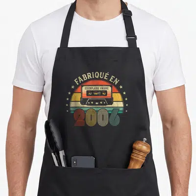 Tablier de cuisine noir avec illustration cassette vintage et texte « fabriqué en 2006 exemplaire unique » sur fond arc-en-ciel délavé.