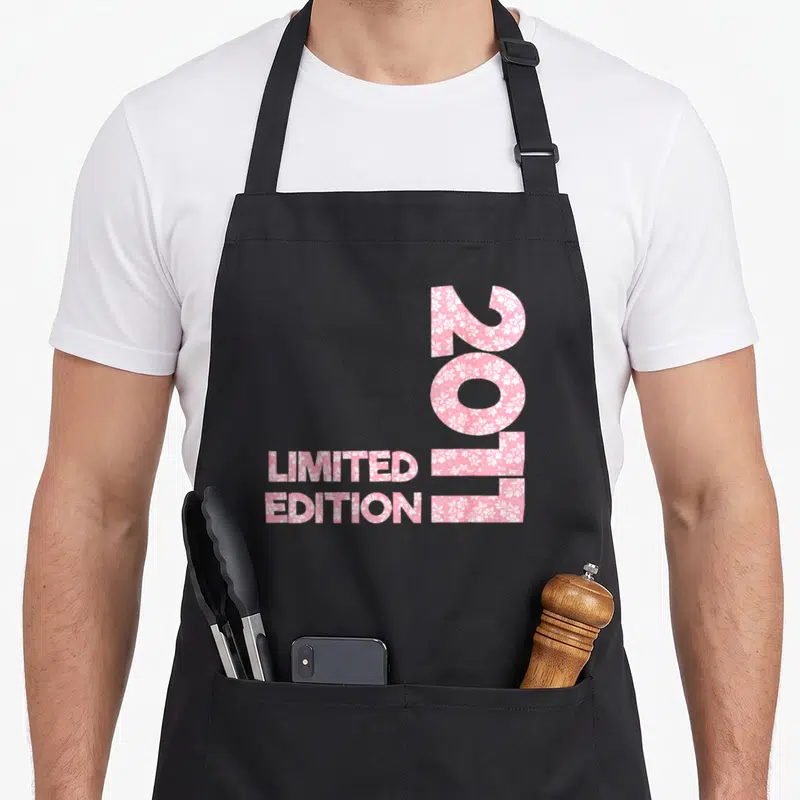 Tablier de cuisine noir avec inscription 2011 Limited Edition remplie de motifs floraux roses et blancs.