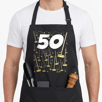 Tablier de cuisine noir avec le chiffre 50 blanc entouré de nombreux balais jaunes à tige bois.
