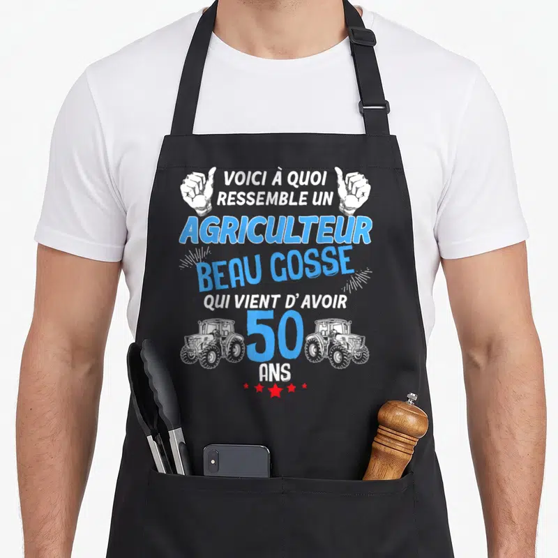 Tablier de cuisine noir avec inscription Agriculteur Beau Gosse 50 Ans et deux tracteurs blancs encadrant le chiffre cent cinquante.