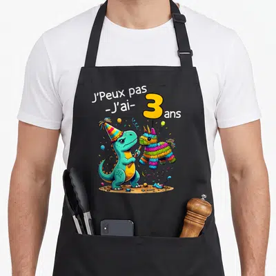 Tablier de cuisine noir avec un dinosaure turquoise portant un chapeau de fête et tenant une pinata colorée.
