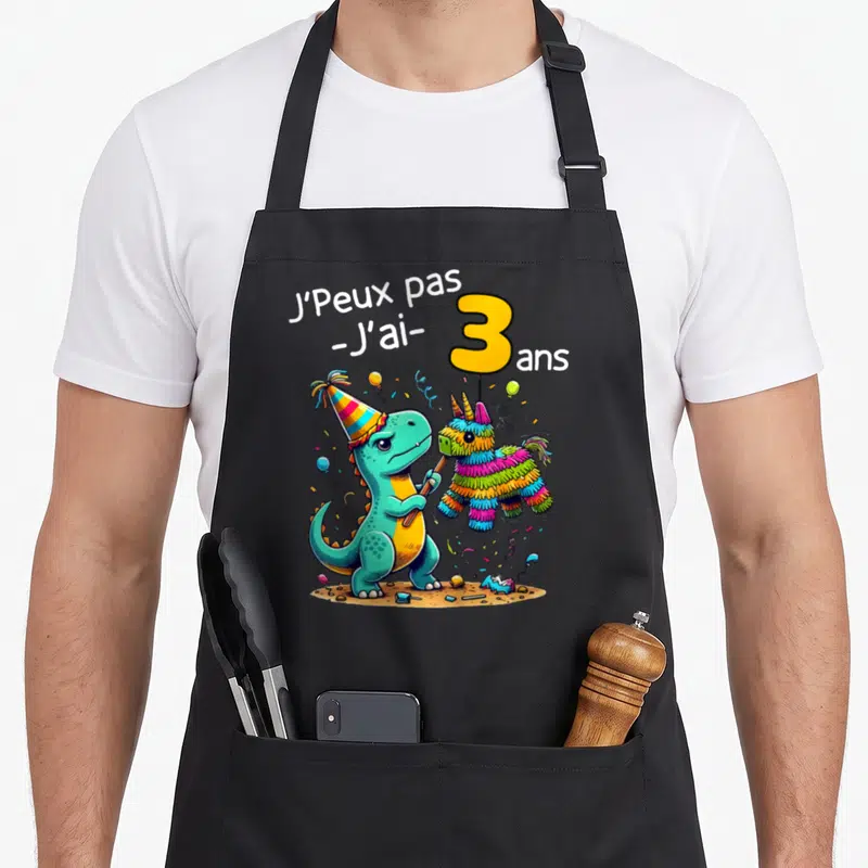 Tablier de cuisine noir avec un dinosaure turquoise portant un chapeau de fête et tenant une pinata colorée.