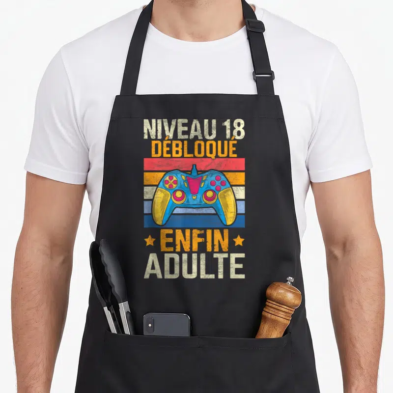 Tablier de cuisine noir avec illustration de manette de jeu vidéo et texte Niveau 18 Débloqué Enfin Adulte en lettres colorées vintage.