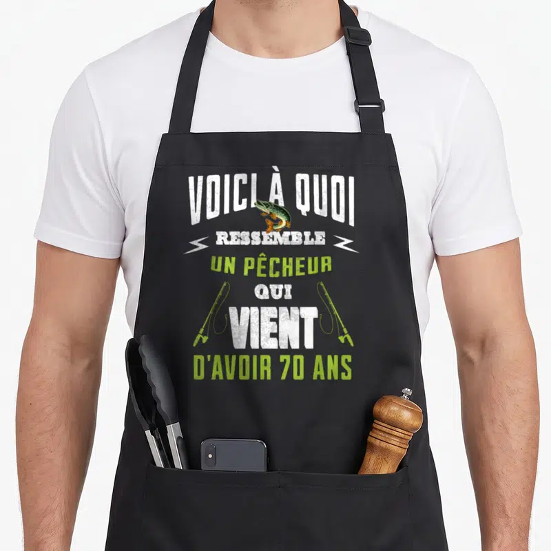 Tablier de cuisine noir avec inscription Voici quoi ressemble un pêcheur qui vient d'avoir 70 ans et illustration de brochet sautant.