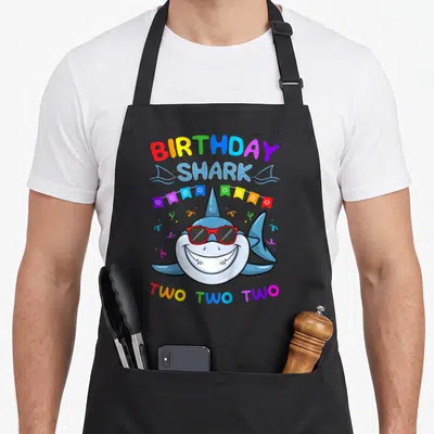Tablier de cuisine noir avec un requin bleu portant des lunettes de soleil rouges et le texte anniversaire Shark Two Two Two.