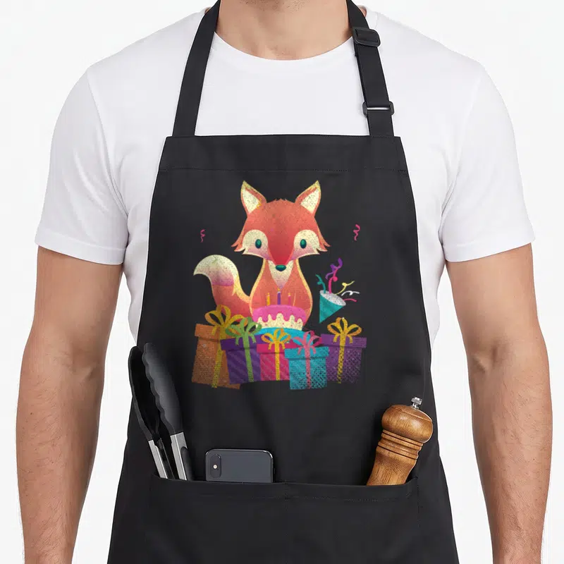Tablier de cuisine noir avec un renard mignon entouré de cadeaux colorés et d'un gâteau d'anniversaire rose.