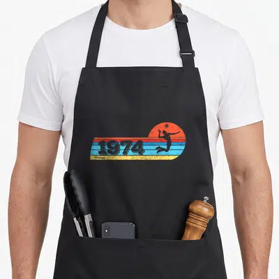 Tablier de cuisine noir avec illustration retro 1974 volley-ball et silhouette de femme en action.