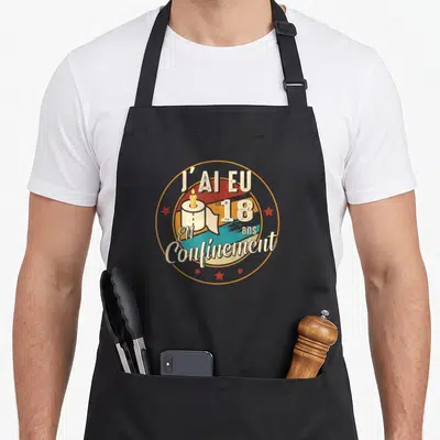 Tablier de cuisine noir avec l'inscription J'ai eu 18 ans en confinement et une illustration de rouleau de papier hygiénique.