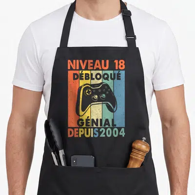 Tablier de cuisine noir avec illustration vintage de manette de jeu vidéo et texte Niveau 18 Débloqué Génial Depuis 2004 sur fond coloré.