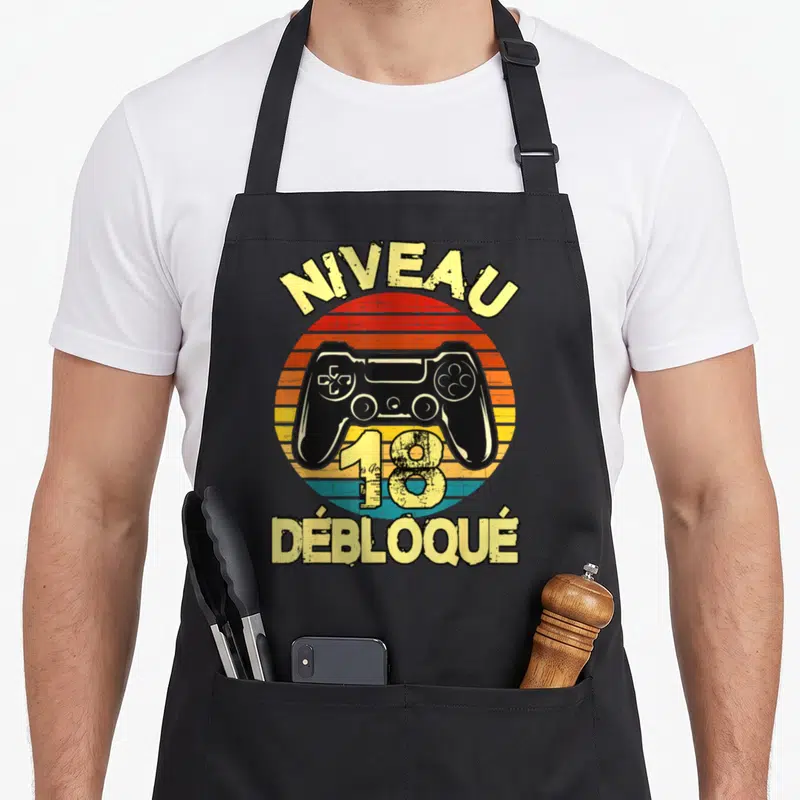 Tablier de cuisine noir avec illustration vintage manette de jeu vidéo et texte Niveau 18 Débloqué en jaune.