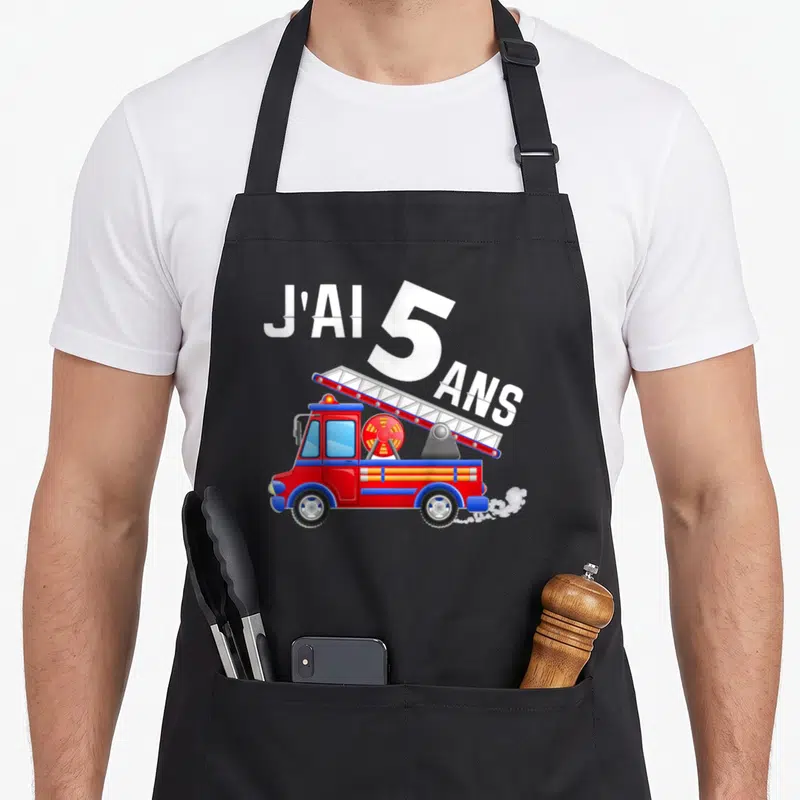 Tablier de cuisine noir avec un camion de pompiers rouge, une échelle et l'inscription J'ai 5 ans en blanc.