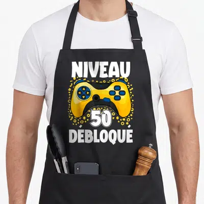 Tablier de cuisine noir avec une manette jaune et le texte Niveau 50 débloqué imprimé en blanc.