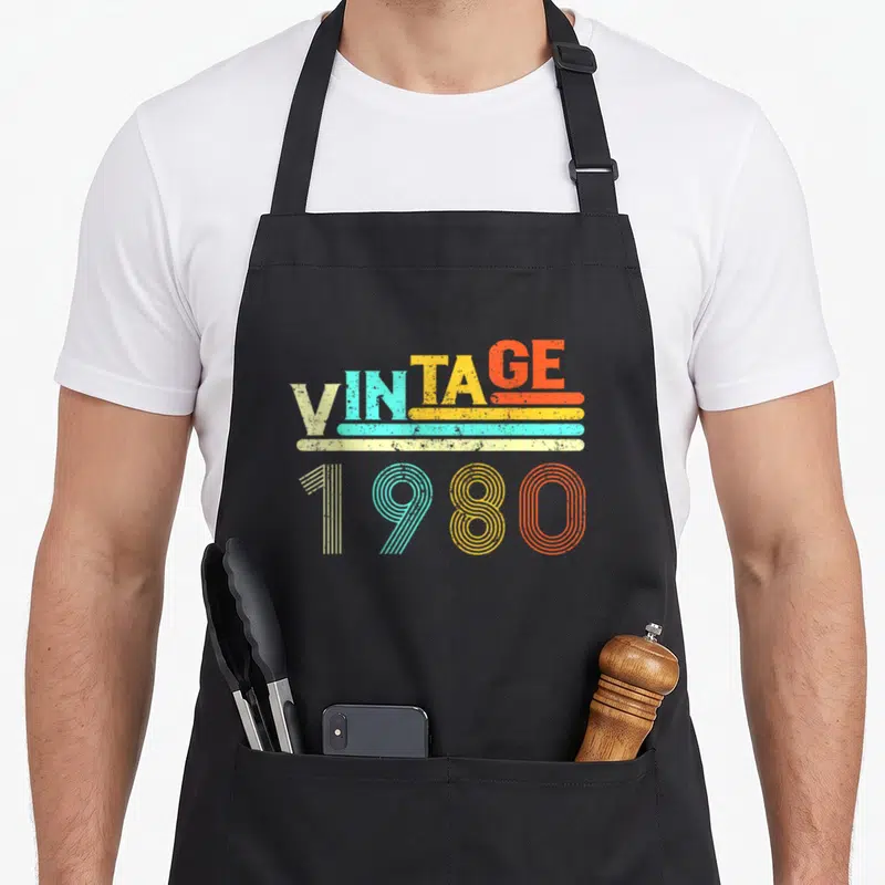 Tablier de cuisine noir avec l'inscription Vintage 1980 en lettres colorées et rayures horizontales sur fond uni.