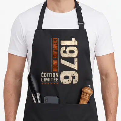 Tablier de cuisine noir avec l'année 1976 et le texte exemplaire unique en typographie vintage orange et crème.