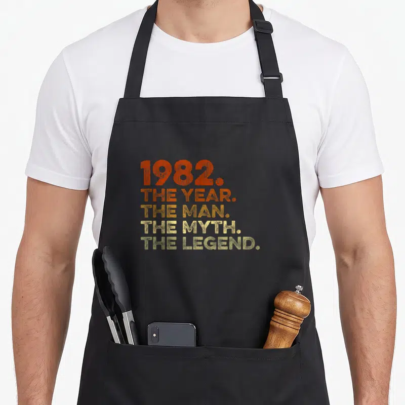 Tablier de cuisine noir avec l'inscription 1982 The Year The Man The Myth The Legend en orange et jaune