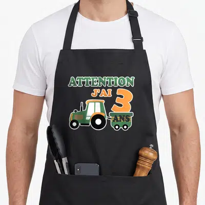Tablier de cuisine noir avec tracteur vert et texte Attention j'ai 3 ans imprimé en couleur.