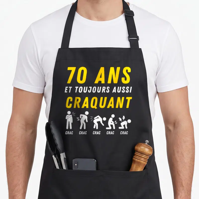 Tablier de cuisine noir avec texte 70 ans et toujours aussi craquant et silhouettes blanches illustrant des cracs.