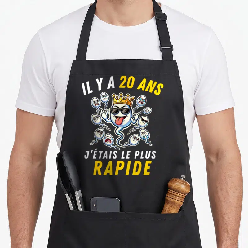 Tablier de cuisine noir avec illustration d'un spermatozoïde couronné et lunettes de soleil entouré de petits personnages.