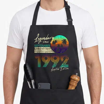 Tablier de cuisine noir avec motif rétro 1992, soleil arc-en-ciel et palmiers stylisés.