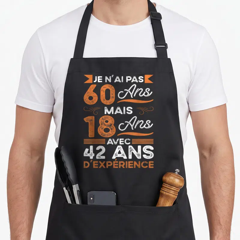 Tablier de cuisine noir avec texte Je n'ai pas 60 ans mais 18 ans avec 42 ans d'expérience en orange et blanc.