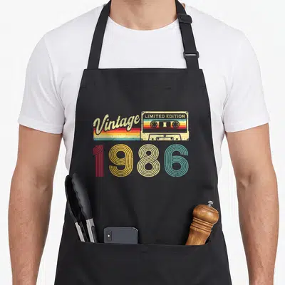 Tablier de cuisine noir avec illustration cassette vintage 1986 et texte limited edition en couleurs pastel.