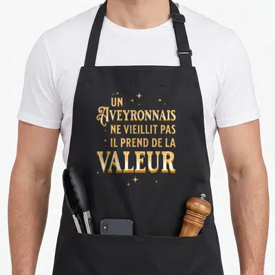 Tablier de cuisine noir avec inscription dorée Un Aveyronnais ne vieillit pas il prend de la valeur entouré d'étoiles scintillantes.