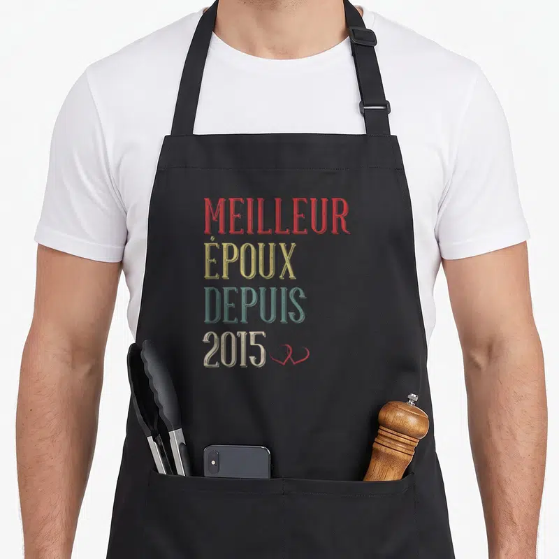 Tablier de cuisine noir avec l'inscription Meilleur Époux Depuis 2015 en lettres colorées et un petit cœur rouge.