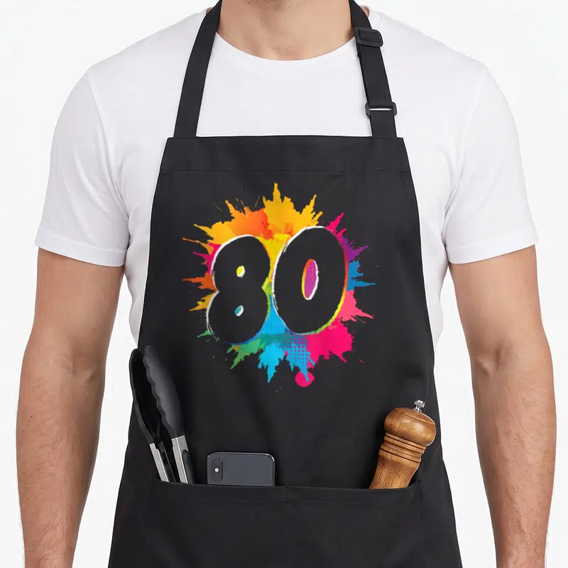 Tablier de cuisine noir avec le chiffre 80 et des éclaboussures de peinture multicolores vives sur le devant.