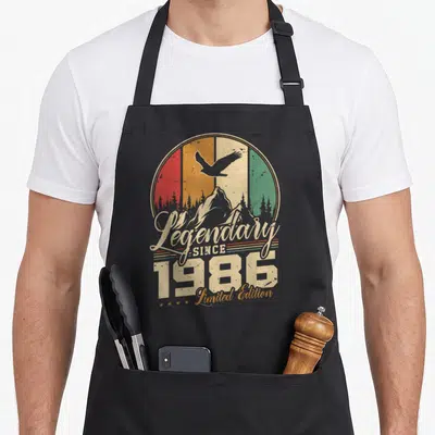 Tablier de cuisine noir avec illustration vintage montrant un aigle en vol au-dessus de montagnes et le texte Légendaire Since 1986 Limited Edition.