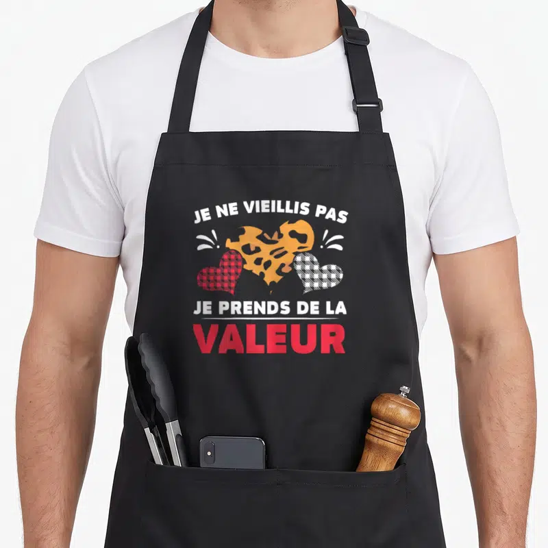 Tablier de cuisine noir avec trois cœurs colorés et texte humoristique sur le devant.