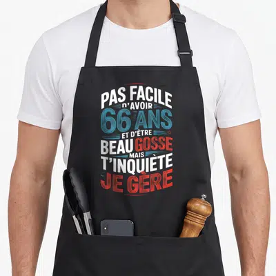Tablier de cuisine noir avec typographie blanche bleue et rouge affichant un message d'anniversaire humoristique pour 66 ans.