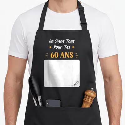 Tablier de cuisine noir avec inscription On signe tous pour tes 60 ans et zone blanche à signer en bas à droite.