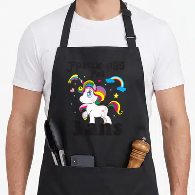 Tablier de cuisine noir avec licorne multicolore, arcs-en-ciel et texte J'peux pas j'ai 3 ans imprimé en gros caractères noirs.