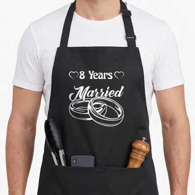 Tablier de cuisine noir avec l'inscription 8 Years Married et deux anneaux entrelacés en blanc.