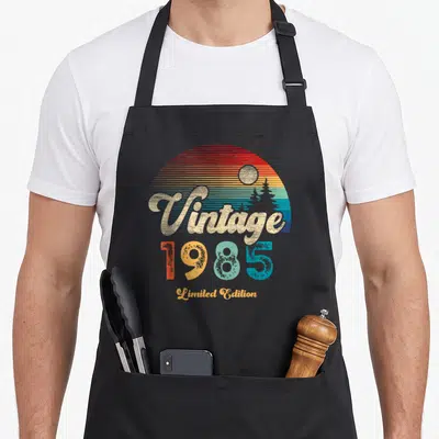 Tablier de cuisine noir avec motif vintage 1985Limited Edition Sunset coloré et lettrage doré stylisé.